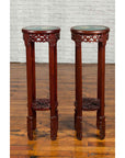 Brown wood Chinese carved round stands with painted floral and bird design on wooden floor against white brick wall.