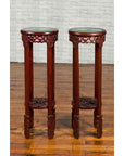 Brown wooden Chinese carved round stands with painted floral and bird designs, displayed on a wooden floor near brick wall.