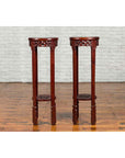 Dark wood carved Chinese round stands with painted floral and bird designs, set against a white brick wall on wood floor.