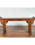 Dark wood Chinese altar console table with carved cloud motifs on wooden floor, white brick wall background.