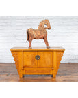 Brown carved wooden horse on Chinese early 20th c. elm sideboard with carved spandrels, white brick wall background.