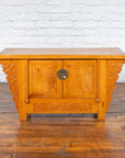 Brown elm Chinese Early 20th Century sideboard with carved spandrels and apron against a white brick wall and wood floor.
