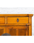 Brown elmwood side chest with bronze medallion hardware, set against a white brick wall.