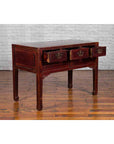 Dark red wood Chinese antique console table with drawers and horse hoof legs, set against a white brick wall.