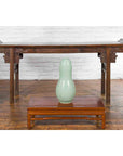 Green glazed ceramic gourd-shaped vase on a curved wooden table with carved legs.
