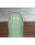 Green glazed ceramic gourd-shaped vase with narrow opening from Chiang Mai, on wooden surface, close-up.