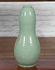 Green glazed ceramic gourd-shaped vase on wooden surface with brick wall background, Prem Collection Chiang Mai.