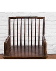Brown elmwood Chinese Qing Dynasty armchair with slatted back and arms, against a white brick wall background.