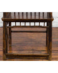 Brown elmwood Qing Dynasty armchair with slatted back and arms, front view on wooden floor against white brick wall.