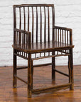 Brown elmwood Chinese Qing Dynasty armchair with slatted back and arms on wooden floor against white brick wall.
