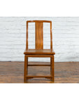 Brown carved elmwood Chinese side chair with rattan seat, set against a white brick wall.