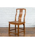 Brown carved elmwood Chinese side chair with rattan seat on a wooden floor beside a white brick wall, early 20th century.