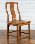 Brown carved elmwood side chair with rattan seat, Early 20th Century Chinese style, on wooden floor by white brick wall.