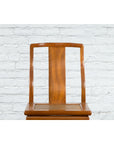 Brown carved elmwood side chair with rattan seat set against a white brick wall background, early 20th-century Chinese.