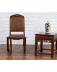 Brown wooden Chinese Qing Dynasty side chair with rattan accents, set against a white brick wall background.
