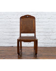 Brown wooden Qing Dynasty side chair with rattan accents on a wood floor against a white brick wall.