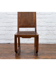 Brown wooden Chinese Qing Dynasty side chair with rattan accents on a wood floor against a white brick wall.