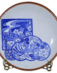 White porcelain Japanese Igezara transferware plate with floral landscape design, displayed on a metal stand, white background.