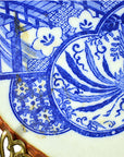 Close-up of a white porcelain Japanese Igezara plate with blue floral and bird designs, metal rim, and clasp.