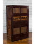 Brown wood Japanese early 20th century Tansu cabinet with sliding doors and drawers against a white brick wall.