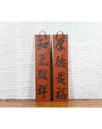 Red and black lacquered wood Chinese calligraphy signs with hand-carved details by a white brick wall.