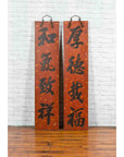 Red and black lacquered wood Chinese signs with hand-carved calligraphy, displayed on a white brick wall.