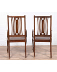 Brown wood vintage Dutch Colonial armchairs with pierced back splats on a wood floor against a white brick wall.