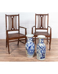 Brown wood Dutch Colonial armchairs on wood floor, white brick wall background with blue-and-white ceramic vases.