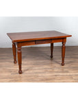 Brown teak antique Dutch Colonial Javanese desk with single drawer and turned legs on wood floor by white brick wall.