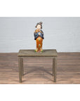 Ceramic figurine on silver overlay Indian vintage metal coffee table in front of a white brick wall.