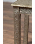 Close-up of silver overlay metal Indian vintage coffee table with floral engraved legs and patterned top on wood floor.