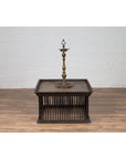 Tall brass candlestick on vintage square Thai rattan coffee table with silver leaf top and spindle design, close-up.