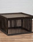 Square rattan coffee table with silver leaf top and spindle design, on wooden floor against a white brick wall.