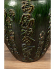 Close-up of green glazed ceramic water jug with calligraphy, on wooden surface.