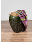 Close-up of green glazed pottery water jug with calligraphy, lidded and draped in colorful patterned scarf.