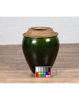 Green glazed ceramic water jug with Chinese calligraphy on wooden floor next to a color chart, contemporary style.