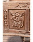 Close-up of natural wood balcony window with hand-carved foliage motifs, bonnet top, and visible wood grain.