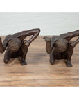 Bronze kneeling table bases with bowed heads and bent arms on a wooden floor against a white wall.
