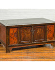 Brown wooden Chinese Qing 19th c. coffee table with painted floral decor and storage, on wooden floor by white brick wall.