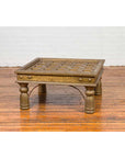 Brown wood and brass coffee table with geometric top and four carved legs, placed on a wooden floor.