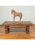 Wooden horse sculpture on brown primitive wood Indonesian coffee table with distressed finish and block legs.