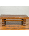 Brown distressed wood Indonesian coffee table with block legs on a polished floor.