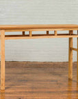 Brown wooden Qing Dynasty console table with pillar strut motifs, four legs, and open shelf on wooden floor.
