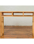Brown wooden Qing Dynasty console table with pillar-shaped strut motifs on a wooden floor against a white brick wall.
