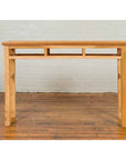 Brown wood Chinese Qing Dynasty console table with pillar-shaped struts, on wooden floor against white brick wall.