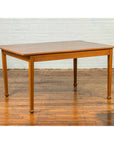 Brown wood vintage Chinese dining table with classical design and spade feet on polished wood floor by white brick wall.