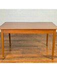 Dark wood vintage Chinese dining table with spade feet on a wooden floor beside a white brick wall.