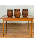 Brown wood vintage Chinese dining table with spade feet, three brown baskets on top, white brick wall background.