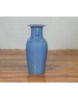 Close-up of blue crackled ceramic altar vase on a wooden floor with a white brick wall background.