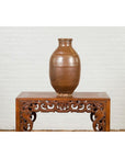 Brown patina water jar from Japanese Meiji period on ornate table, white brick wall background, 19th century.